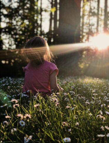 girl sitting on daisy flowerbed in forest