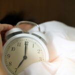 A close-up of a hand reaching for a ringing alarm clock, symbolizing waking up in the morning.